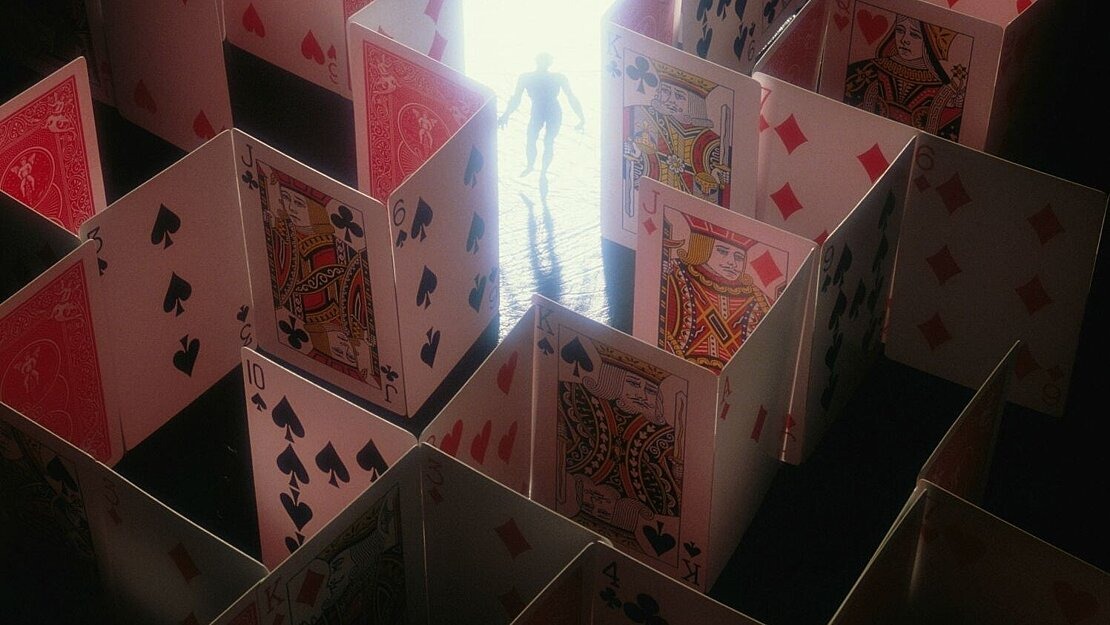 Eine Person steht in einem Labyrinth aus aufgestellten Spielkarten, das von hinten beleuchtet ist – symbolisch für die Lenkung durch Designmuster im Online-Glücksspiel.